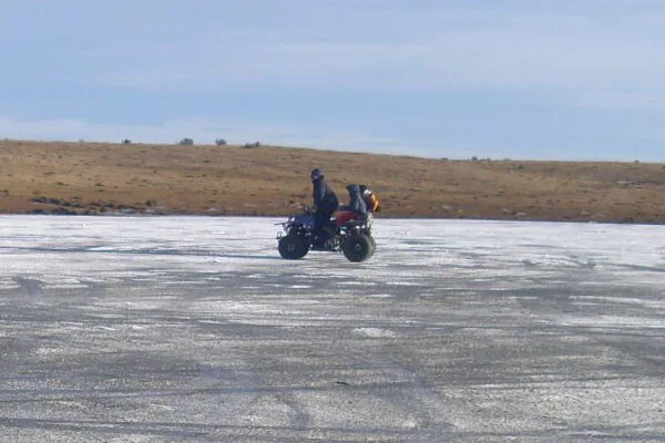 Sin cascos, dos chicos circulan con un cuatriciclo arriba del hielo.